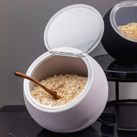 White container with a wooden spoon inside, filled with oats on a dark surface.